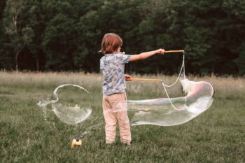 Kind spielt mit riesigen Seifenblasen im Garten