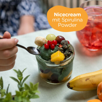 Hand mit Löffelt nähert sich der Spirulina Nicecream in einer Schüssel