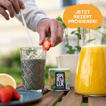 Glas mit grünem Spirulix Smoothie neben Krug mit Orangensaft