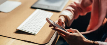 Frau sitzt am Schreibtisch udn hält Smartphone