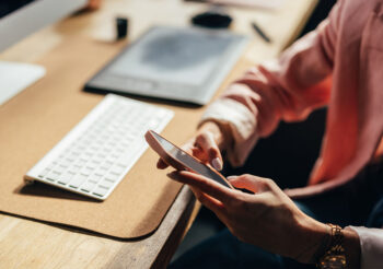 Frau sitzt am Schreibtisch udn hält Smartphone