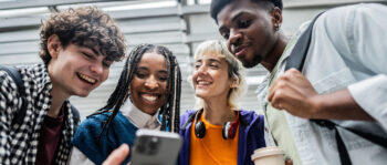 Vier junge Menschen schauen auf ein Smartphone und lachen