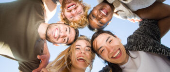 Fünf junge Erwachsene stehen im Kreis, blicken in die Kamera und lächeln strahlend in den klaren Himmel. Sie fangen den fröhlichen Teamgeist ein, der oft in erfolgreichen Performance-Marketing-Kooperationen zu finden ist.